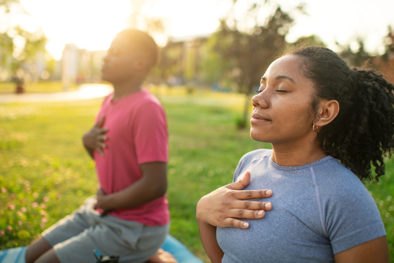 Young couple practicing yoga in a summer park, doing breathing exercise Managing Stress With Yoga